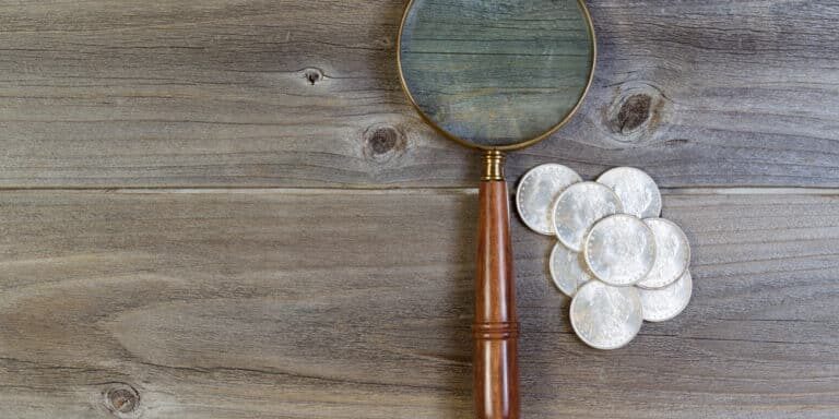 Horizontal view of an antique round shaped magnifying glass and a pile of old silver dollar coins on rustic wood